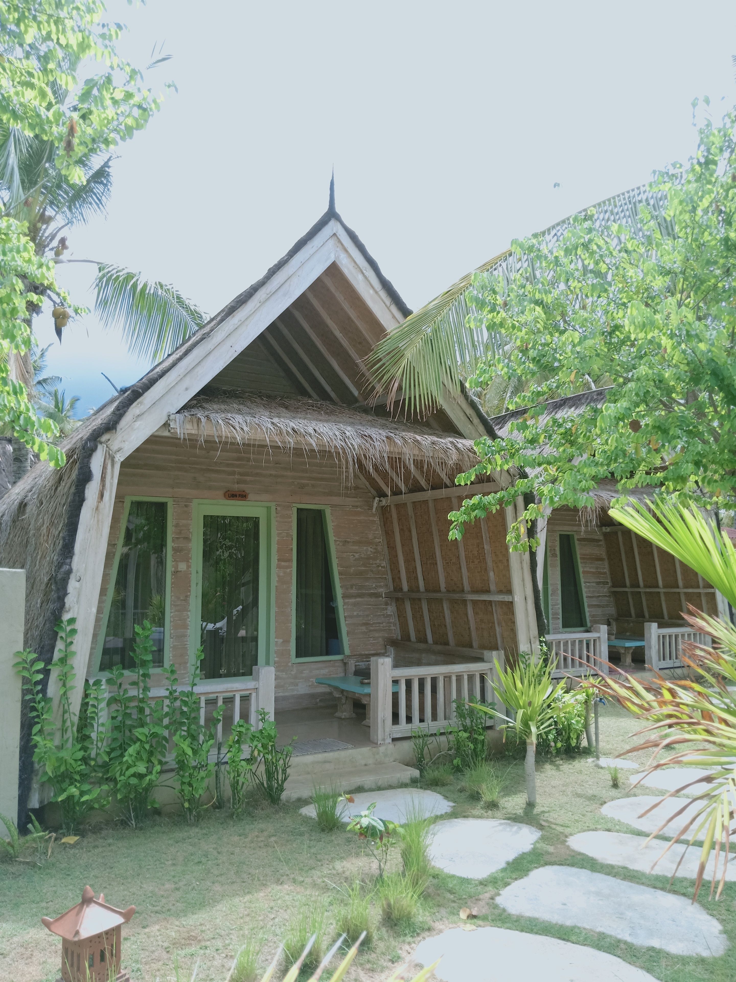 A bungalow with a thatched roof, wooden walls, and a porch with benches.