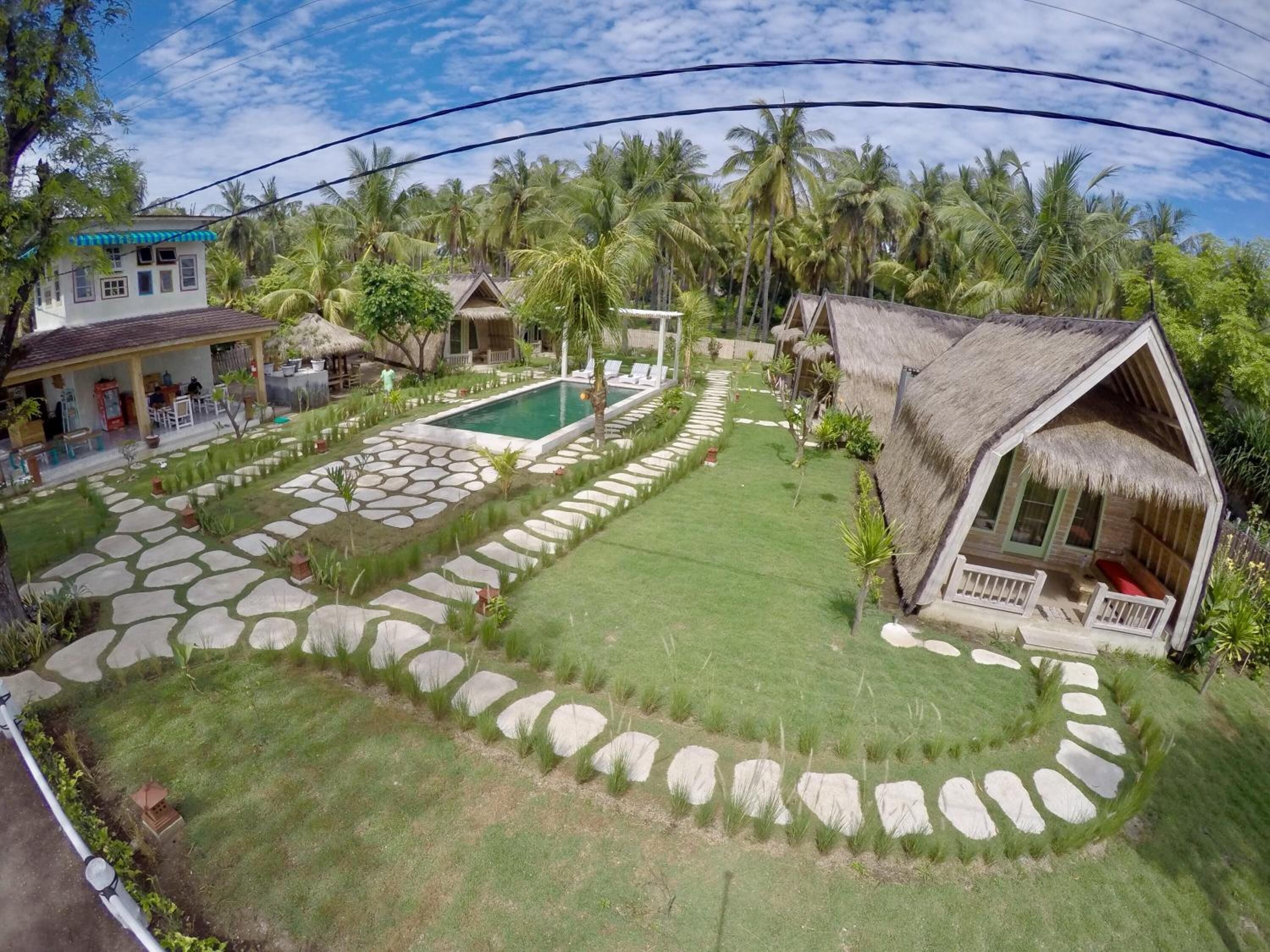 Un resort tropical con piscina, senderos de piedra y construcciones de techo de paja.