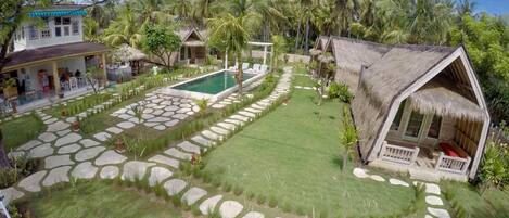 Un resort tropical con piscina, senderos de piedra y construcciones de techo de paja.