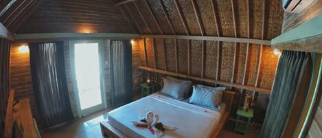 Een gezellige slaapkamer met een houten plafond, een groot bed en een nachtkastje met een lamp.