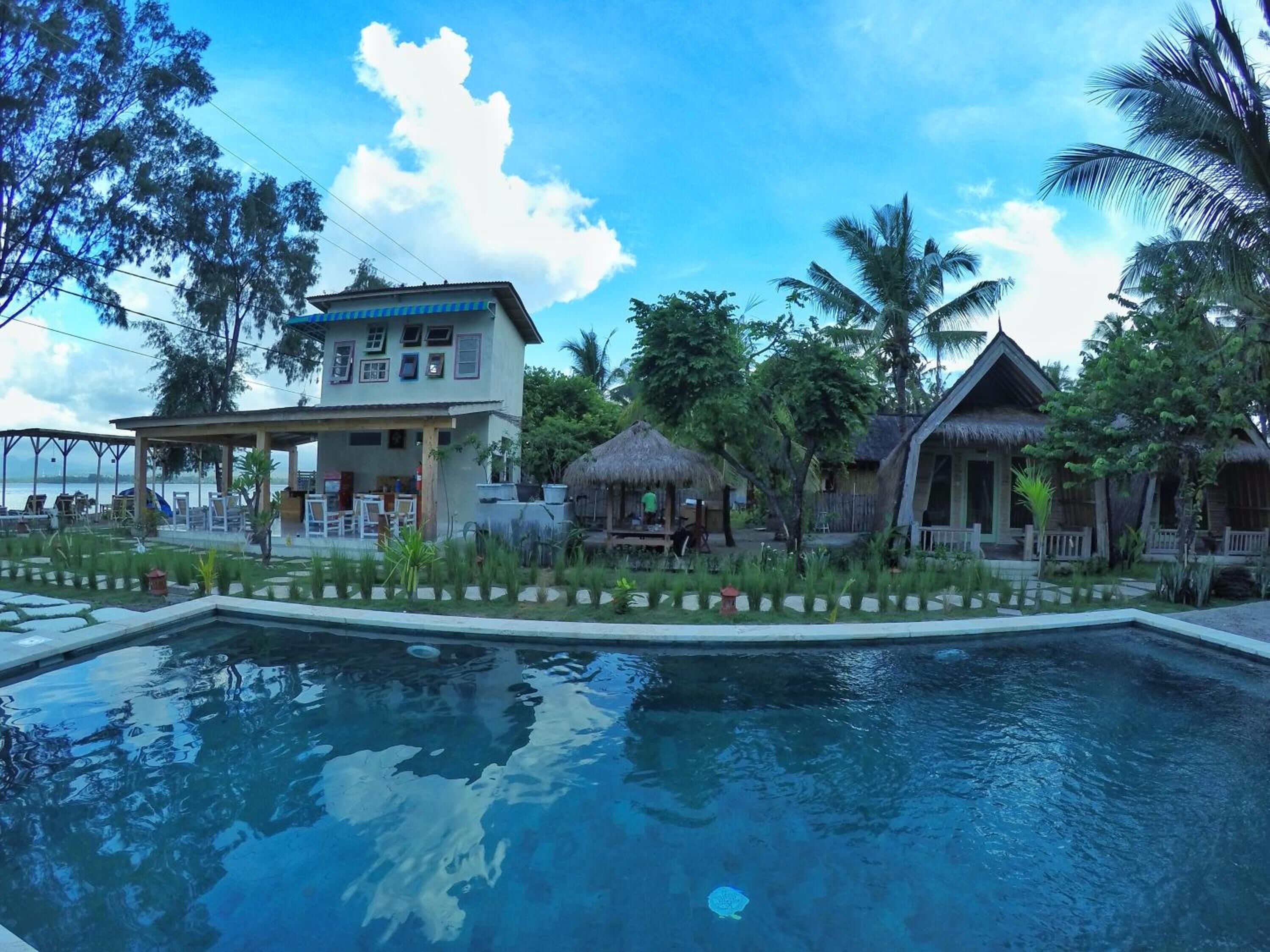Un resort con piscina, construcciones de techo de paja y vegetación tropical.