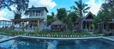 Un resort con piscina, construcciones de techo de paja y vegetación tropical.