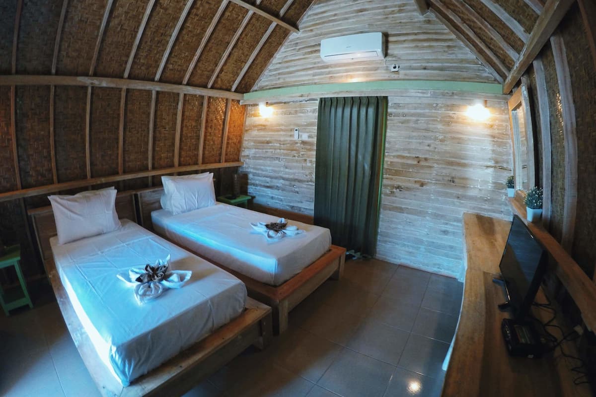Una habitación acogedora con dos camas, techo de madera, cortina verde y un televisor sobre un mueble de madera.