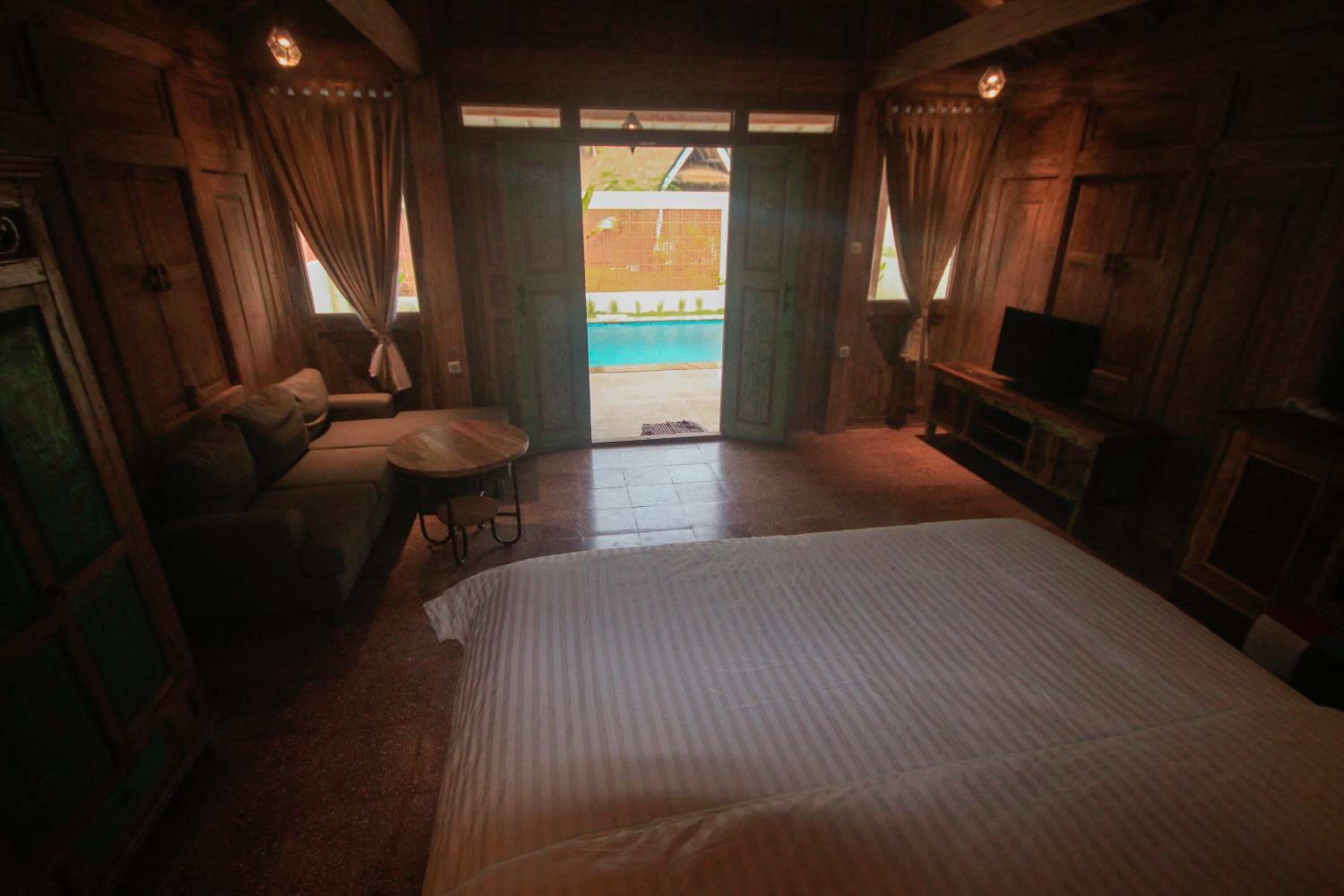 A wooden room with a bed, a sofa, a small table, and a TV.