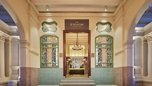 Una entrada imponente con mostrador de recepción, puertas decoradas con un llamativo patrón verde y blanco, y un letrero que dice "The Edison".