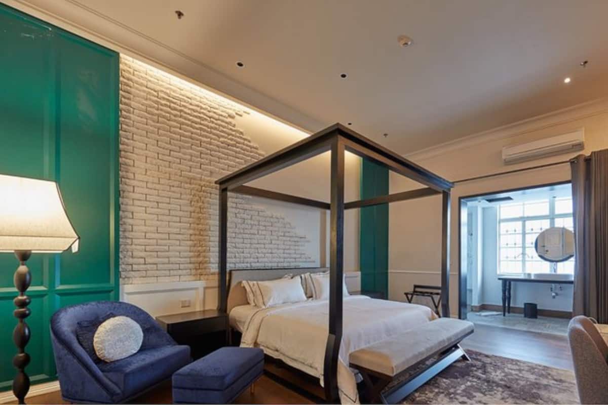 A modern hotel room with a four-poster bed, a green accent wall, a large window, and a view of the city.