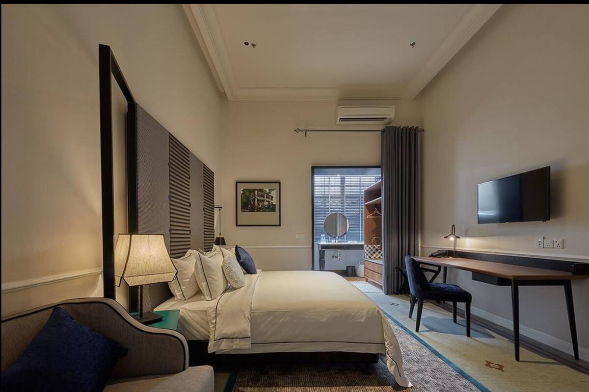 A hotel room with a bed, a desk, a chair, a TV, and a window with blinds.