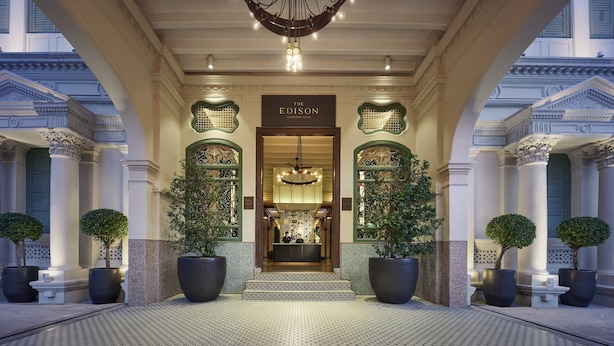 Una entrada imponente con un cartel que dice "The Edison", destacando grandes árboles en macetas, un piso de baldosas y elementos arquitectónicos clásicos.