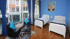 Habitación de hotel con dos camas, un sofá negro, una mesita con un florero y vistas al balcón exterior.