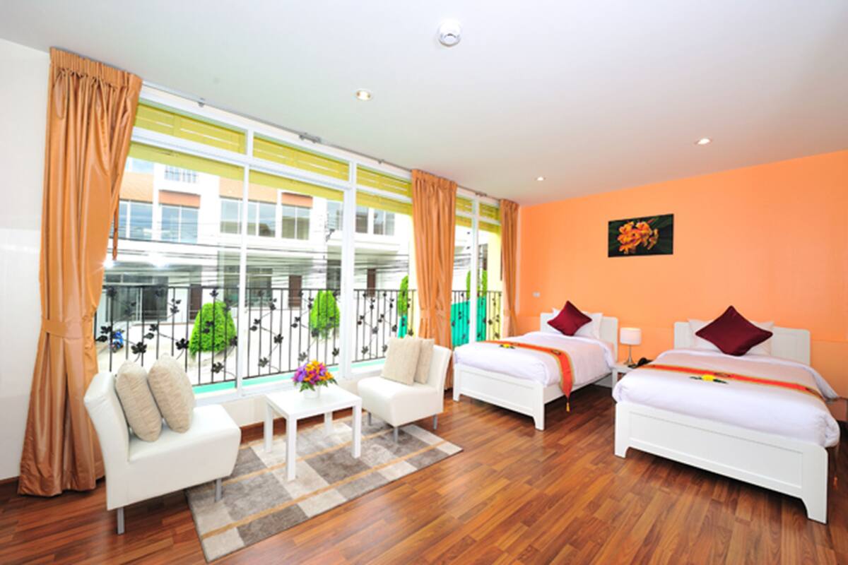 A hotel room with two beds, a sofa, a small table, and a balcony with plants.