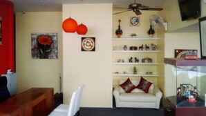 Una sala de estar con un sofá blanco, una mesa de centro de madera, un ventilador de techo y estantes con objetos decorativos.