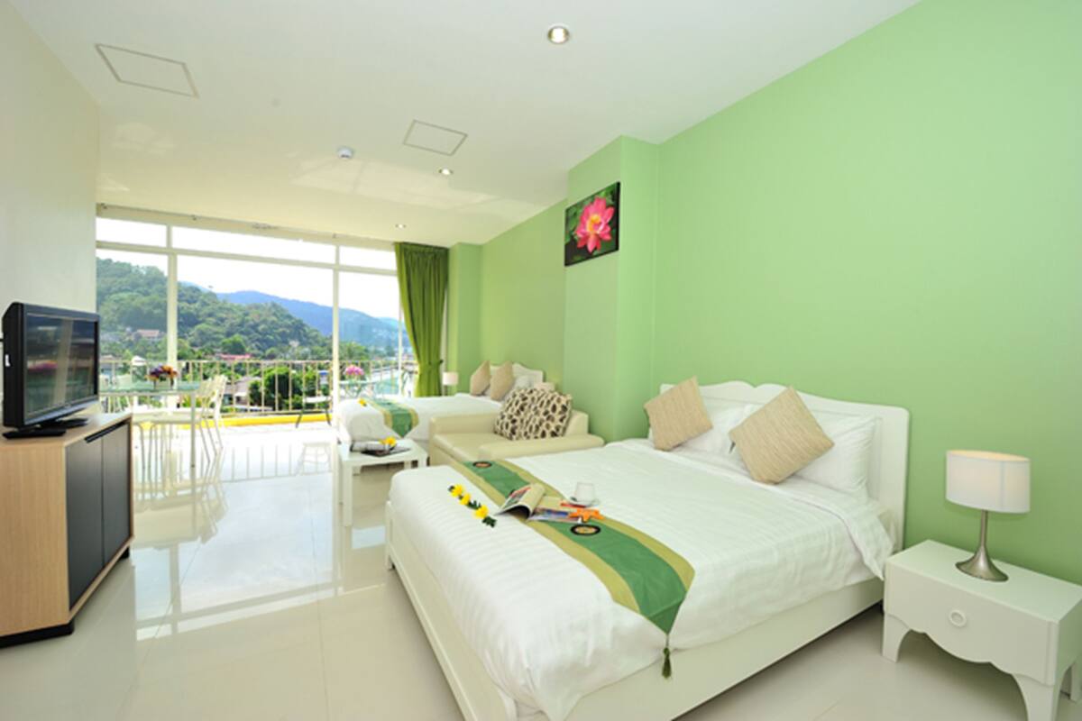 A hotel room with a bed, a TV, a desk, and a balcony with a view of the mountains.