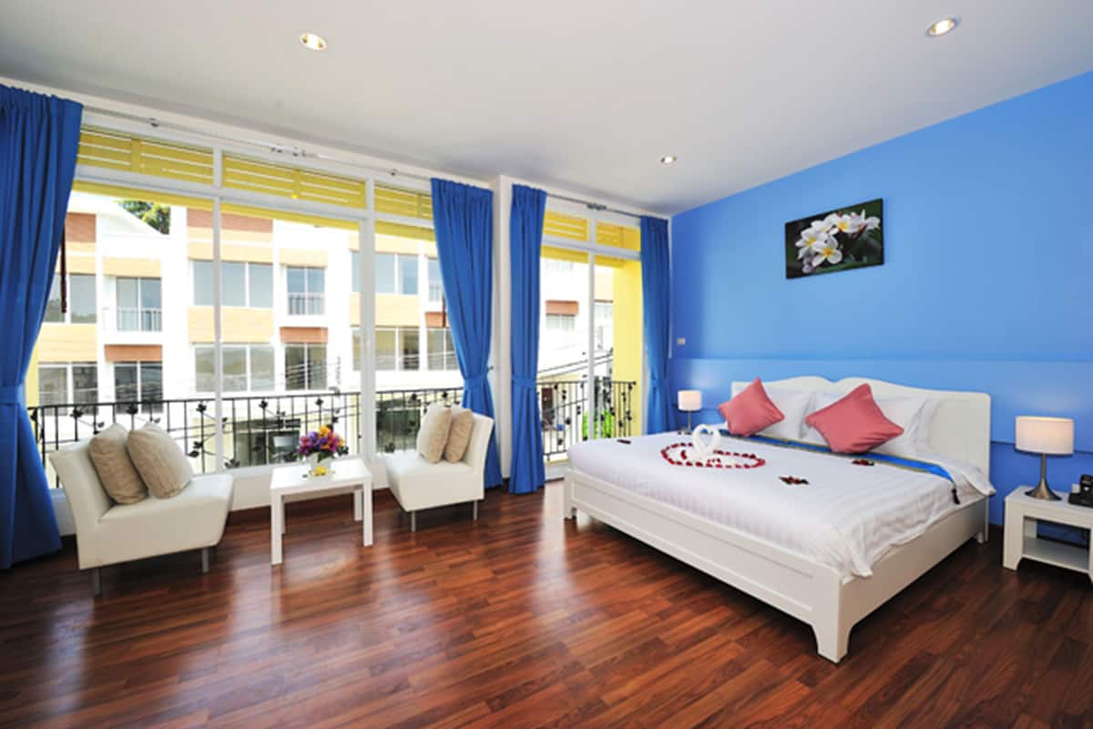A hotel room with a bed, a sofa, a small table, and a balcony with blue curtains.