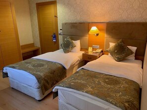 A hotel room with two beds, a wooden wardrobe, a nightstand with a lamp, and a patterned wall. - Adana Yukselhan Hotel (Adana)