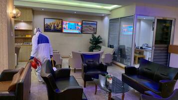 Een hotel lobby met leren banken, een receptiebalie, een kerstboom en een tv waarop nieuws wordt vertoond.