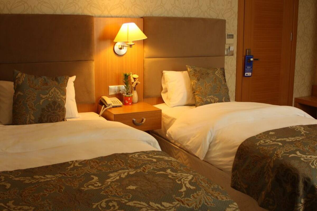 Ein Hotelzimmer mit zwei Betten, einem Nachttisch mit Lampe und einem Holzschrank.