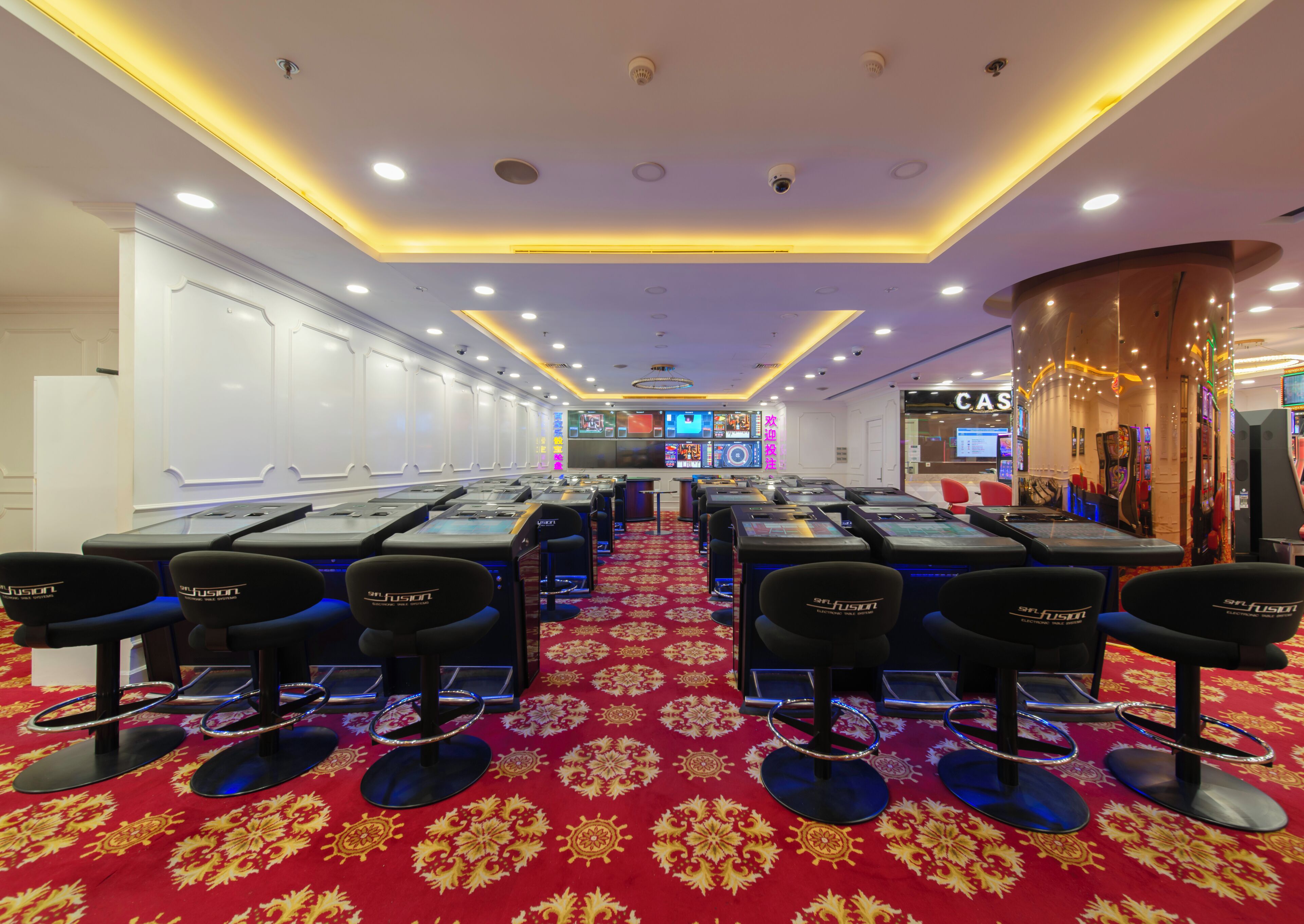 Ein Casino mit mehreren Spieltischen, Stühlen, einem roten Teppich und einer Überwachungsanlage.