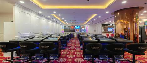Un casino con múltiples mesas de juego y sillas, alfombra roja y un sistema de videovigilancia.