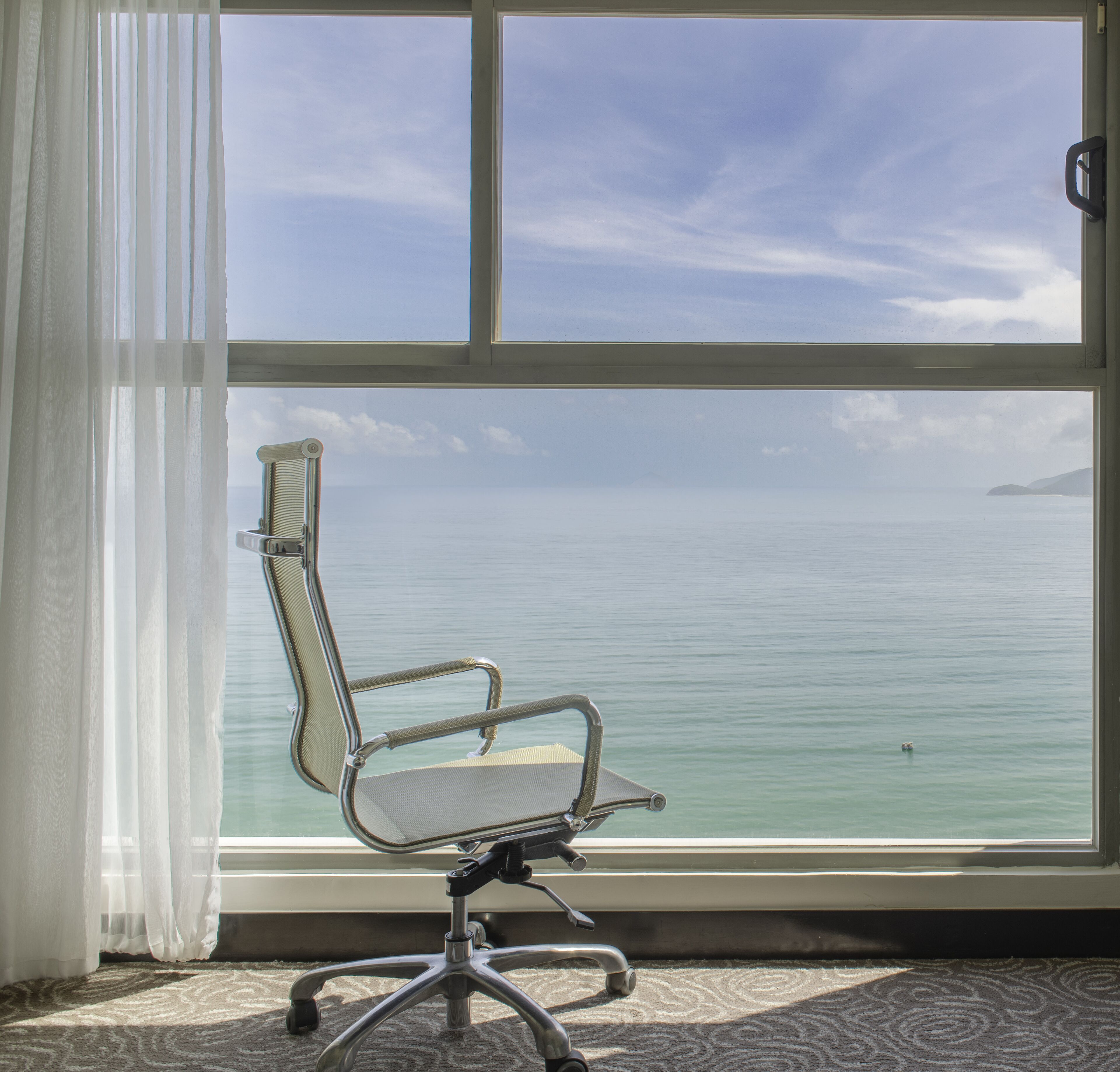 A chair by a window with a view of the sea.