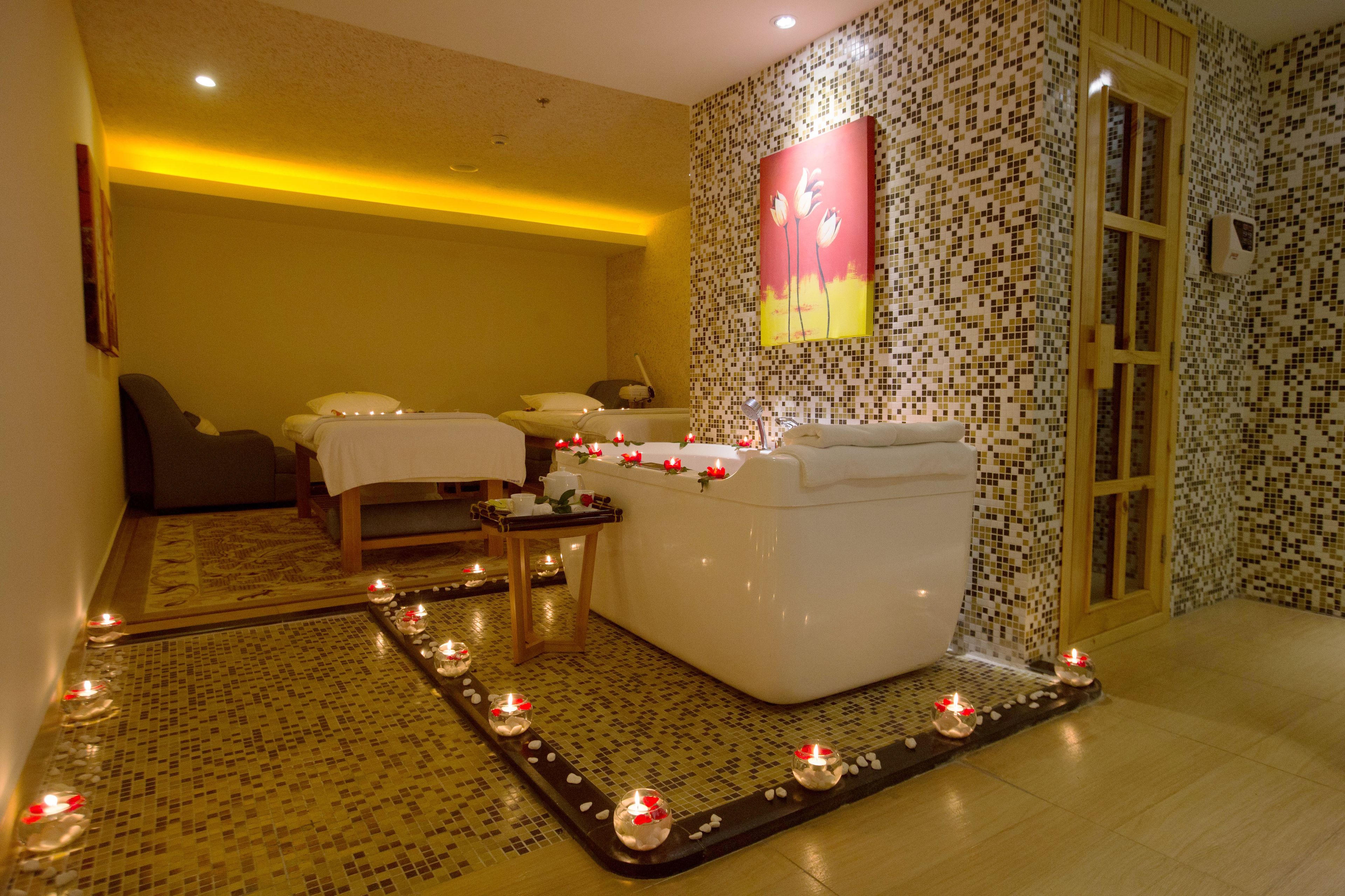 Une salle de spa équipée d’une table de massage, d’une baignoire et d’un mur recouvert de mosaïques.