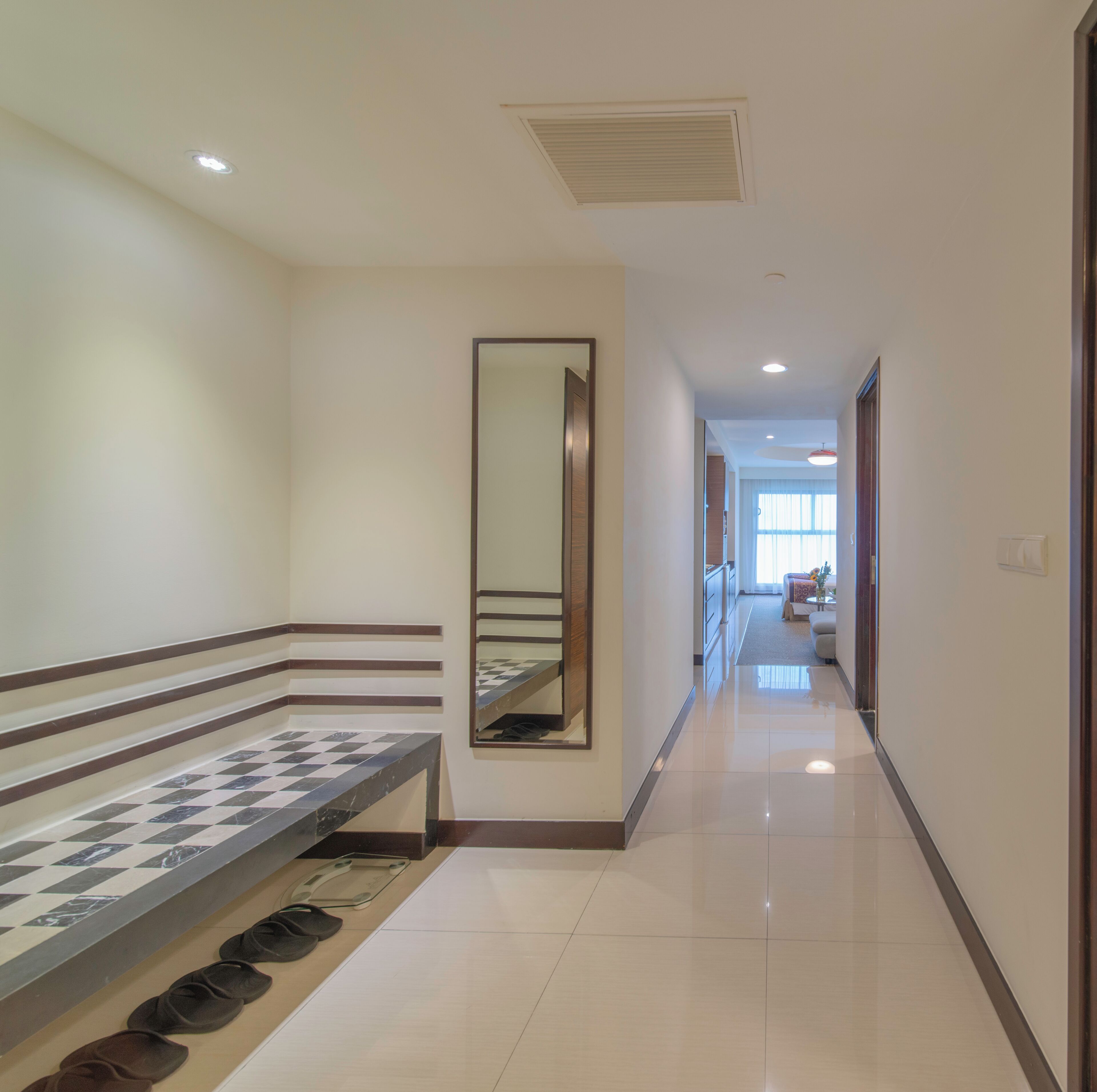 Un couloir d’hôtel avec un sol à carreaux, un miroir et un banc.