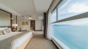 Une chambre d’hôtel dotée d’un grand lit, d’un coin salon, d’une vue sur la mer et d’une porte donnant sur une autre pièce.