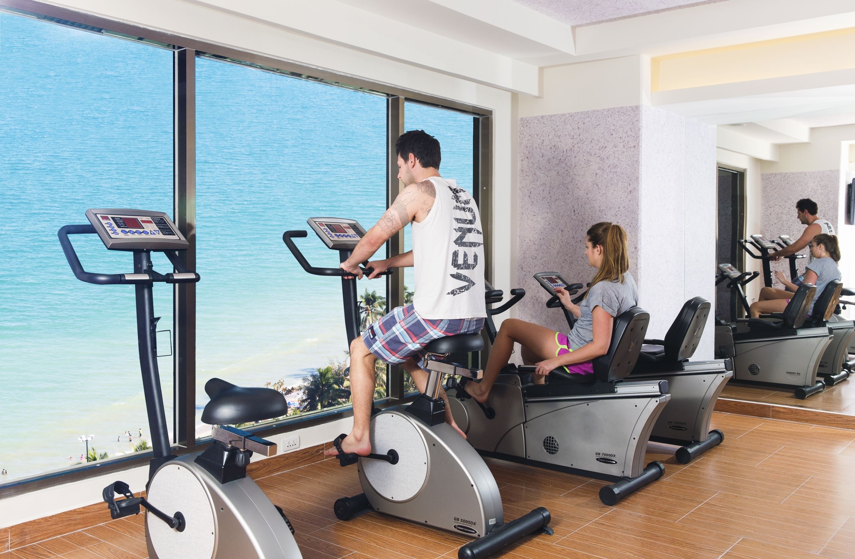 A gym with stationary bikes and a large window overlooking a beach.
