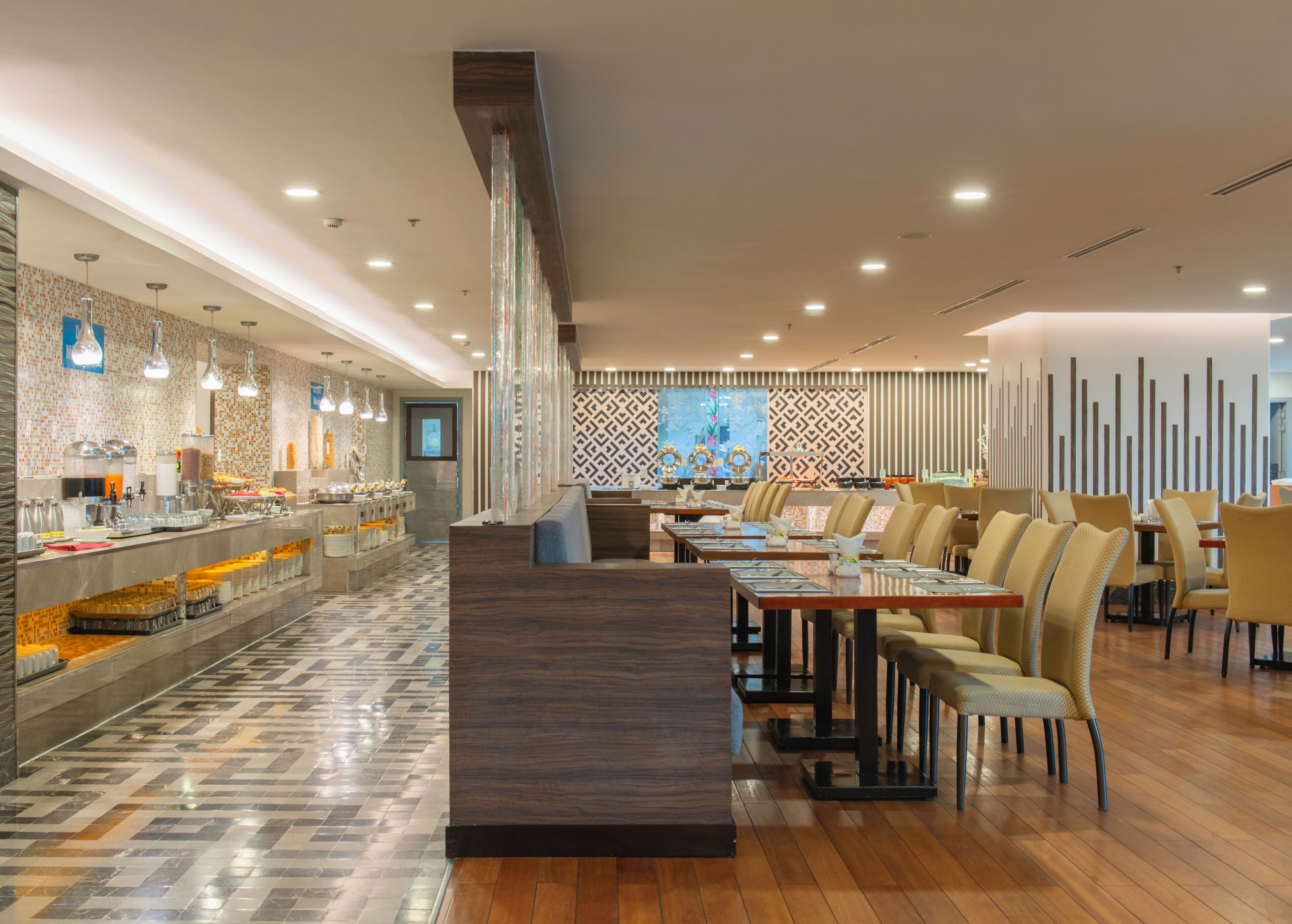 A modern restaurant with a long counter, multiple tables, and a patterned wall in the background.