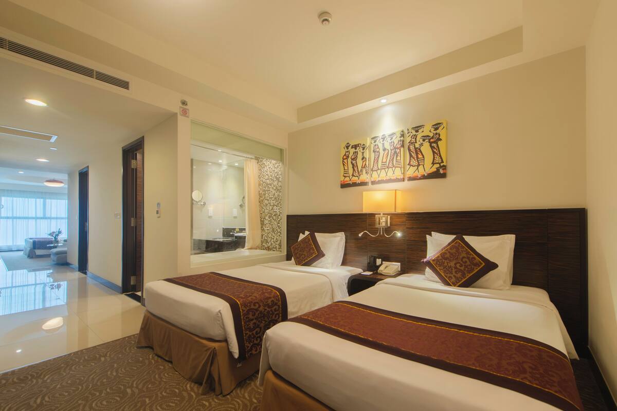 A hotel room with two beds, a bathroom, and a view of the hotel lobby.