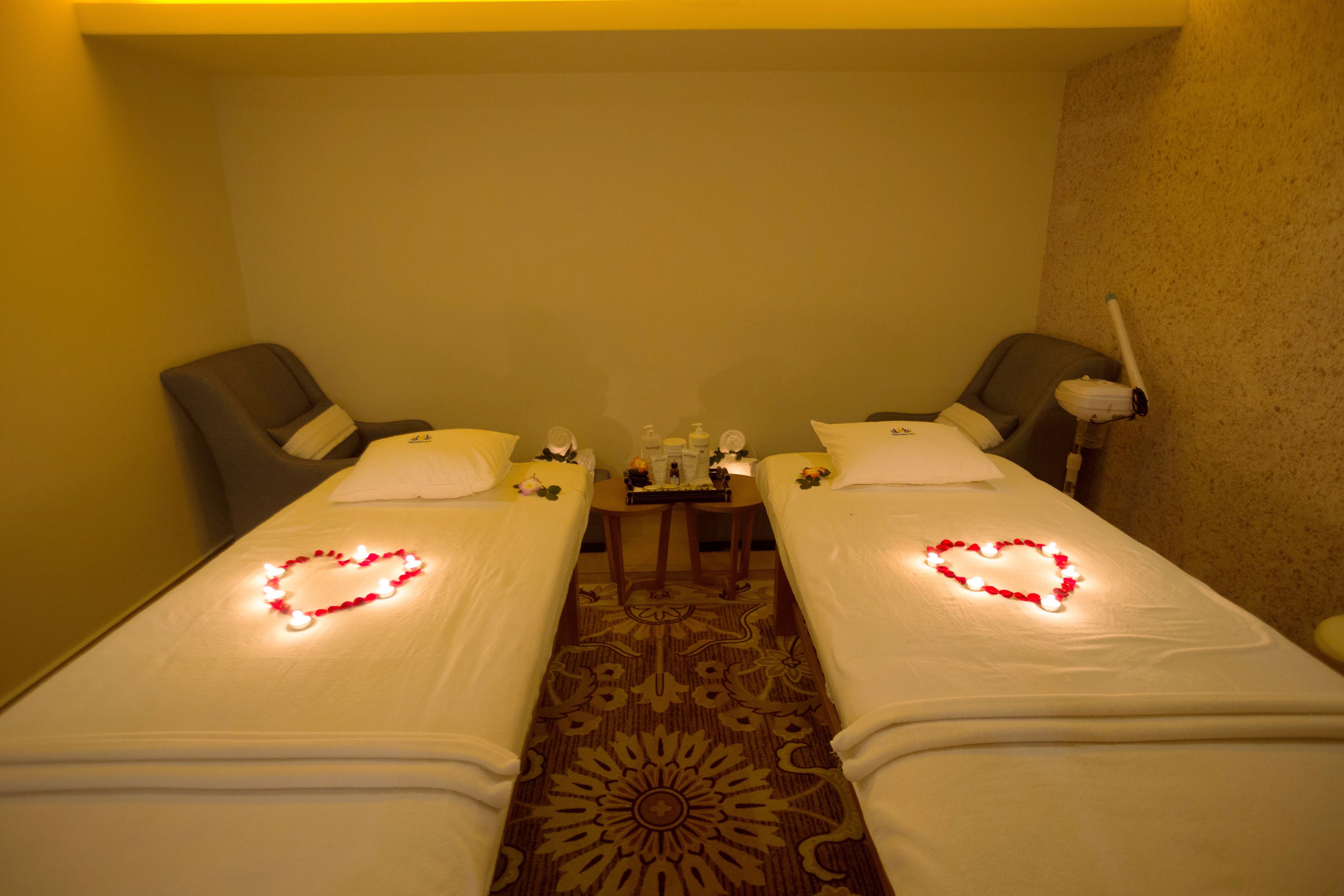 A hotel room with two single beds, each decorated with a heart-shaped light arrangement. There is a small table with toiletries between the beds.