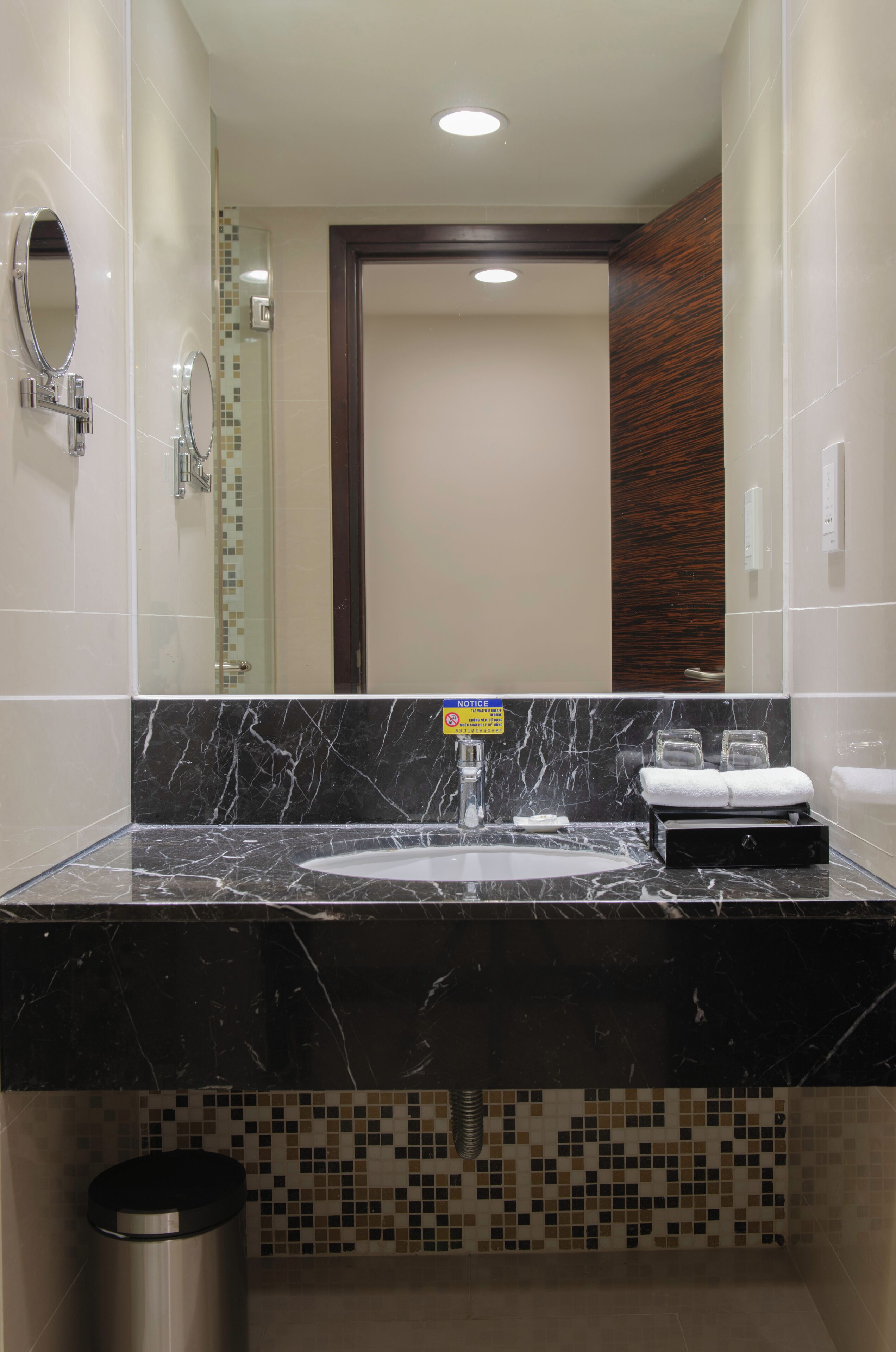 A modern bathroom with a black marble countertop, a glass shower enclosure, and a visible trash bin.