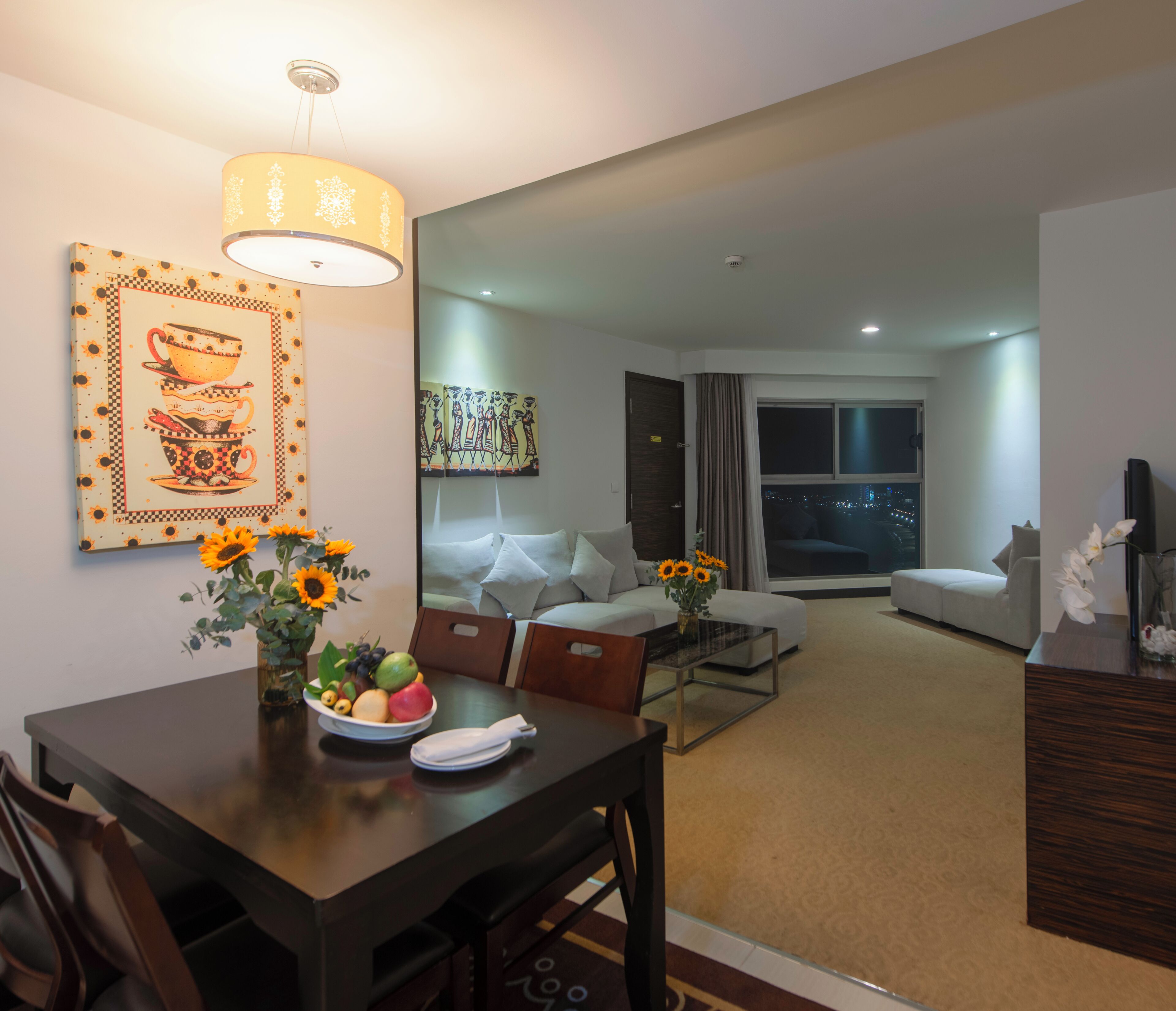 A modern hotel room with a dining area, a sofa, and a large window with a city view.