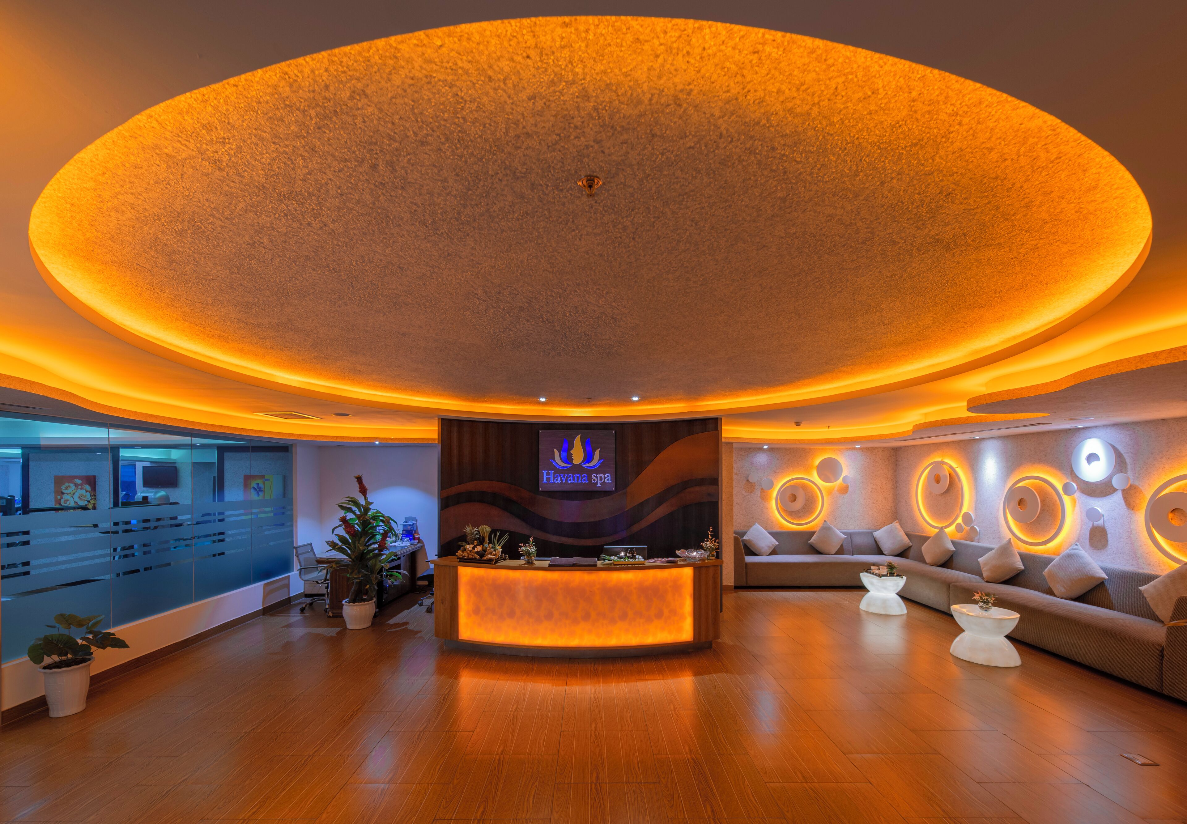 A modern spa reception area with a curved ceiling, a reception desk, seating area, and a wall with circular light patterns.
