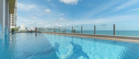 Une piscine d’un bleu éclatant, séparée du reste par une paroi de verre, d’où l’on peut admirer un plan d’eau et des bâtiments au loin.
