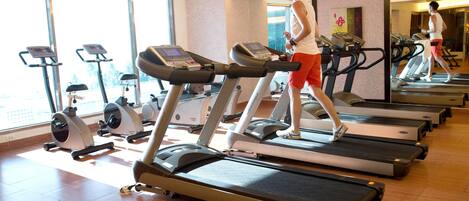 A gym with multiple treadmills, exercise bikes, and a large window providing natural light.