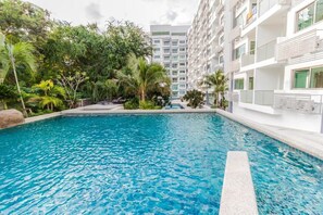 A swimming pool surrounded by lush greenery and modern buildings. - Club Royal Wongamat by PSR ASIA (Pattaya)