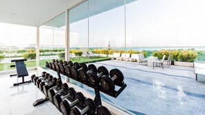 A gym with a row of dumbbells and a bench, overlooking a landscaped area with chairs and a view of the city. - Club Royal Wongamat by PSR ASIA (Pattaya)