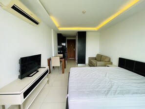 A modern hotel room with a large bed, a TV on a stand, a sofa, and a small desk.