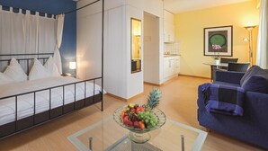 Habitación de hotel con cama, mesa de comedor con fruta, sofá y zona de cocina.