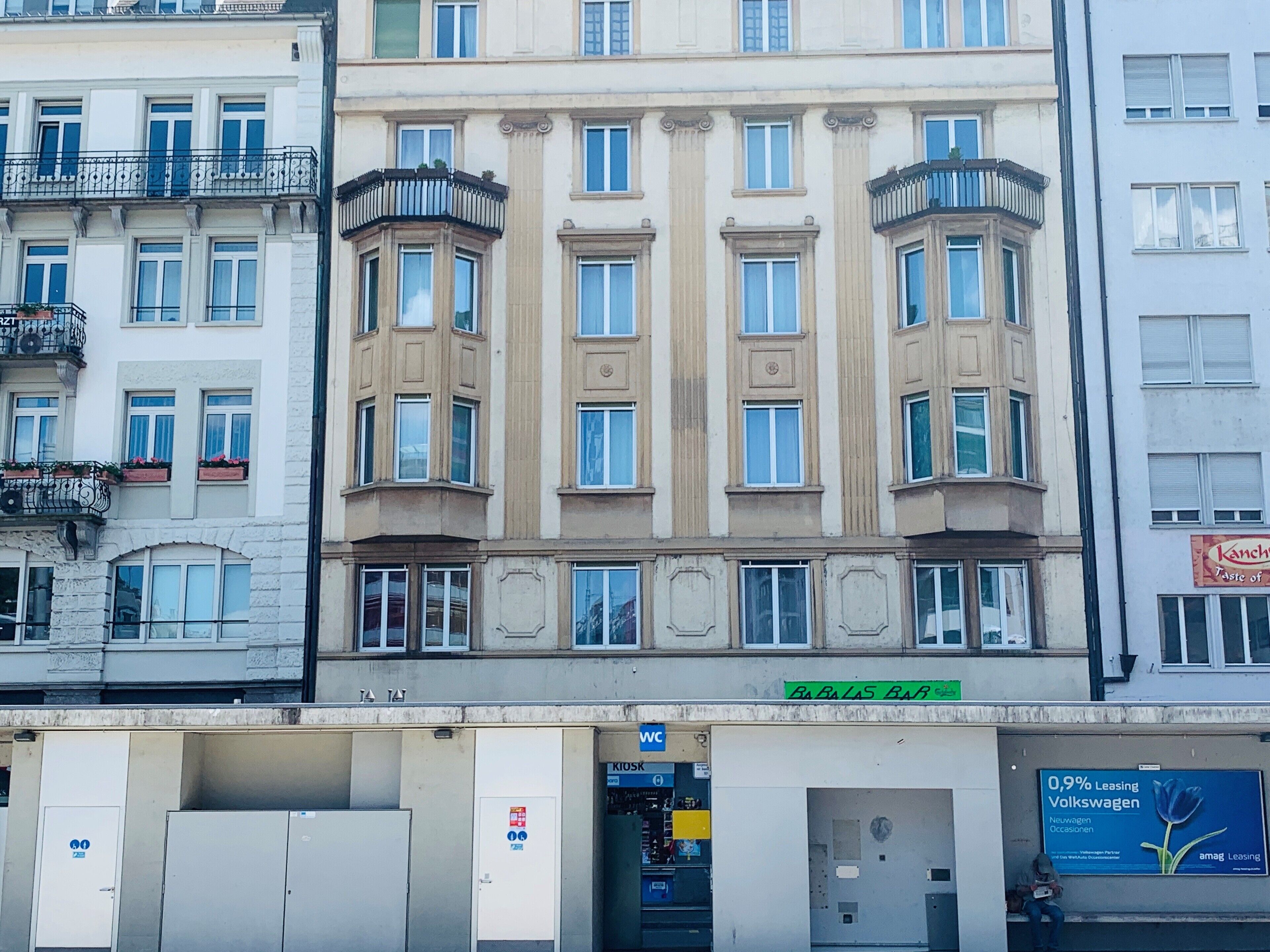 Ein mehrgeschossiges Gebäude mit einem zentralen Eingang, großen Fenstern und einem Schild für "Bablas Bar".