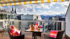 Une terrasse sur le toit, avec des fauteuils en osier, une table et une vue sur la ville et les montagnes.
