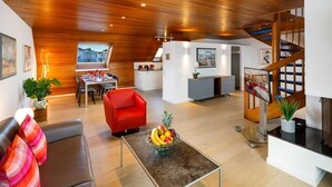 Un salon moderne avec un plafond en bois, un fauteuil rouge, une table basse en verre sur laquelle on peut voir des fruits, et un escalier.
