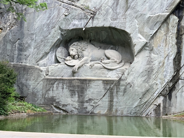 A stone relief of a lion lying down with a shield and spear, surrounded by a rocky wall with inscriptions. - Annex Luzernerhof (Lucerne)
