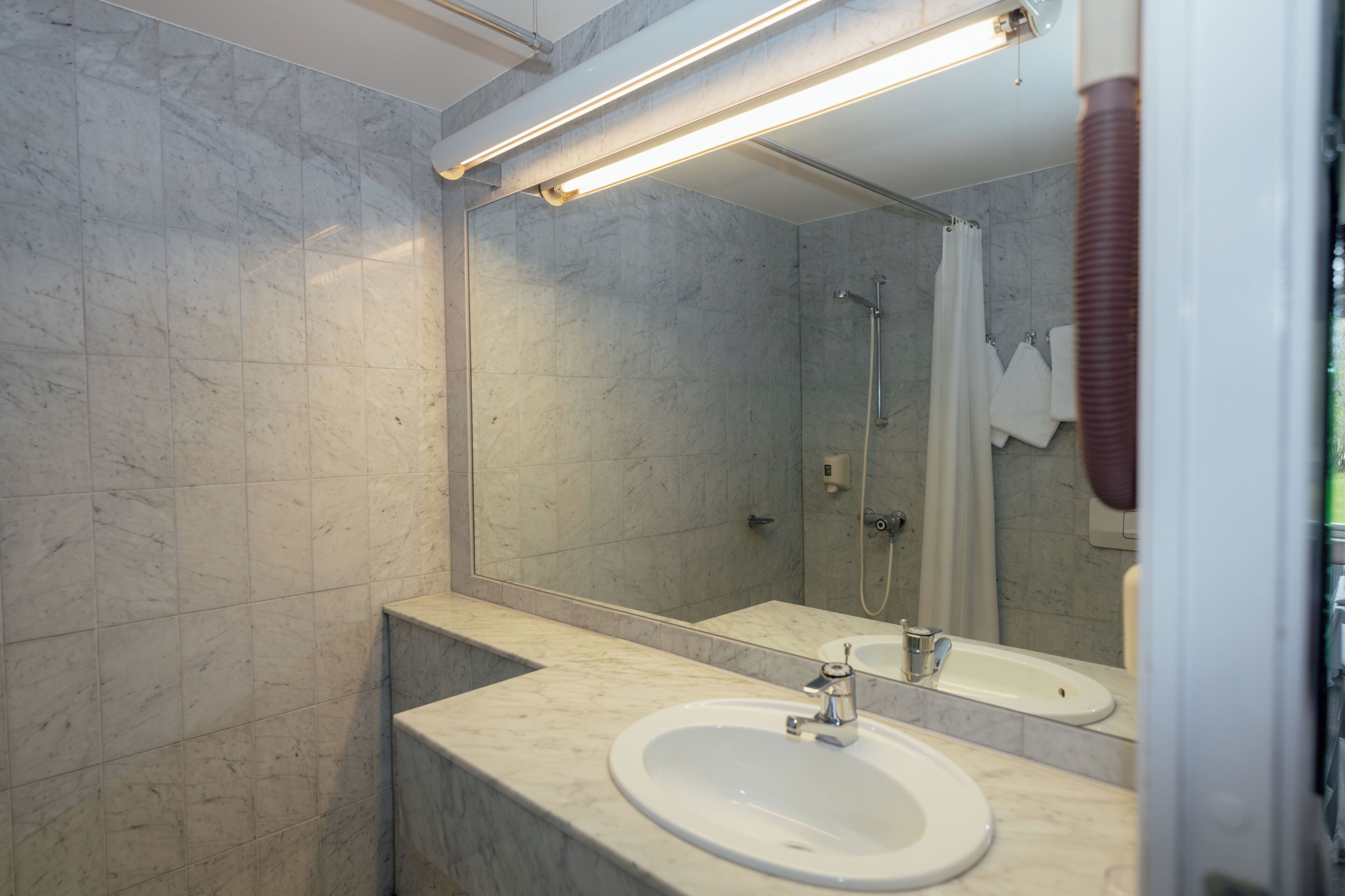A modern bathroom with a marble sink, a large mirror, and a shower area.