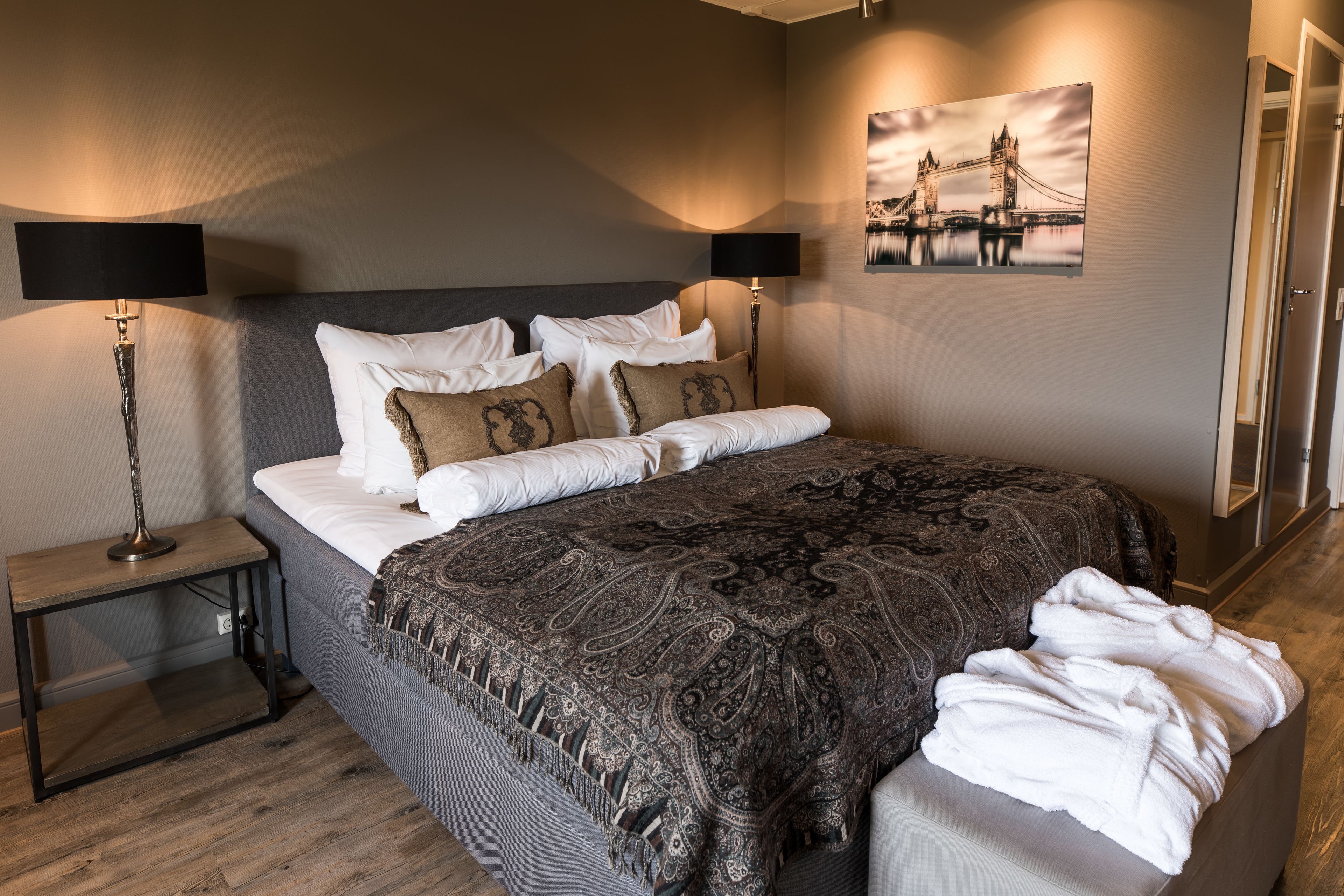 A neatly made bed with a patterned blanket, two bedside lamps, and a framed picture of a bridge on the wall.