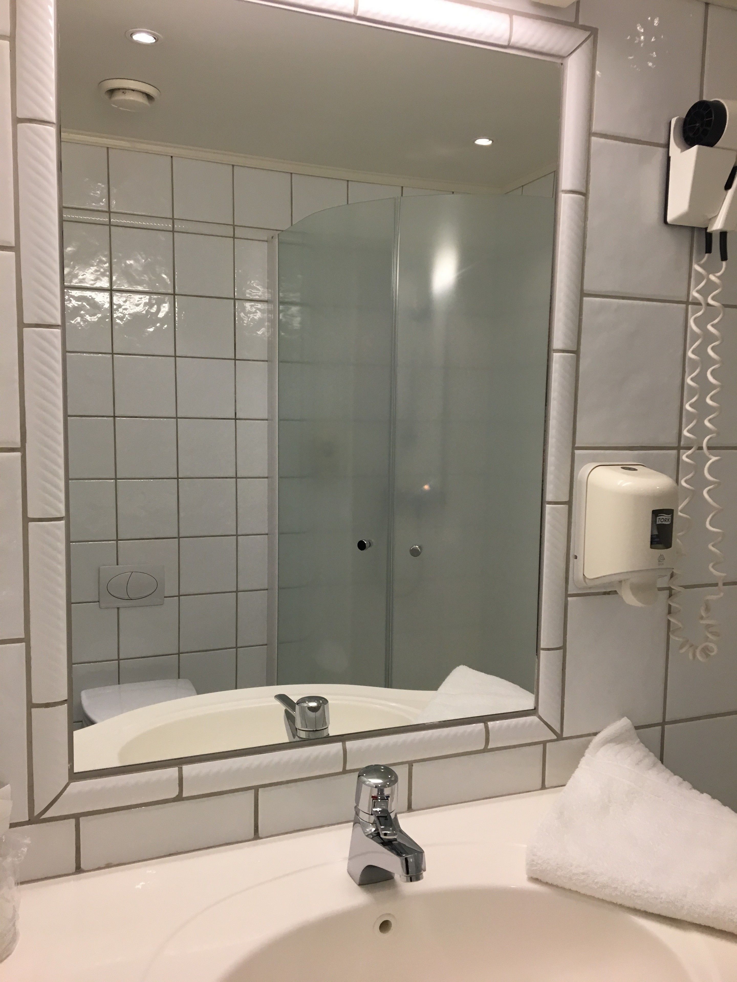 A bathroom with a large mirror, a sink with a modern faucet, a handheld showerhead, and a soap dispenser on the wall.