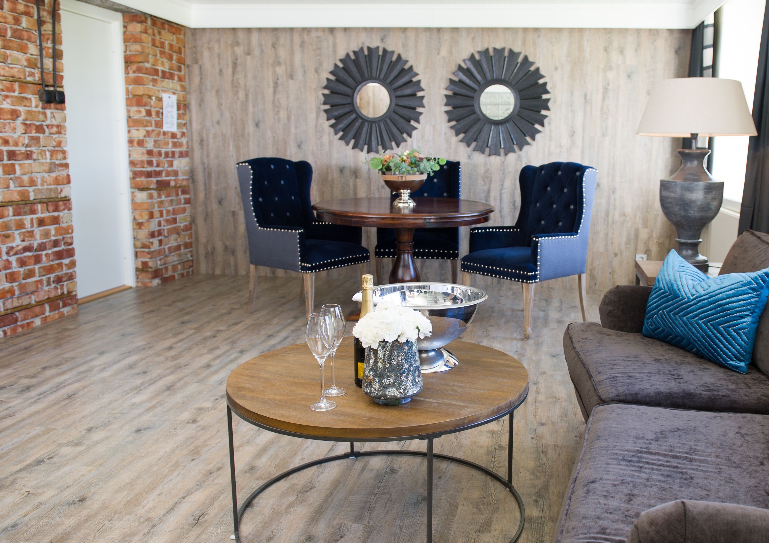 A dining area with a round wooden table, two upholstered chairs, a decorative mirror, and a lamp.