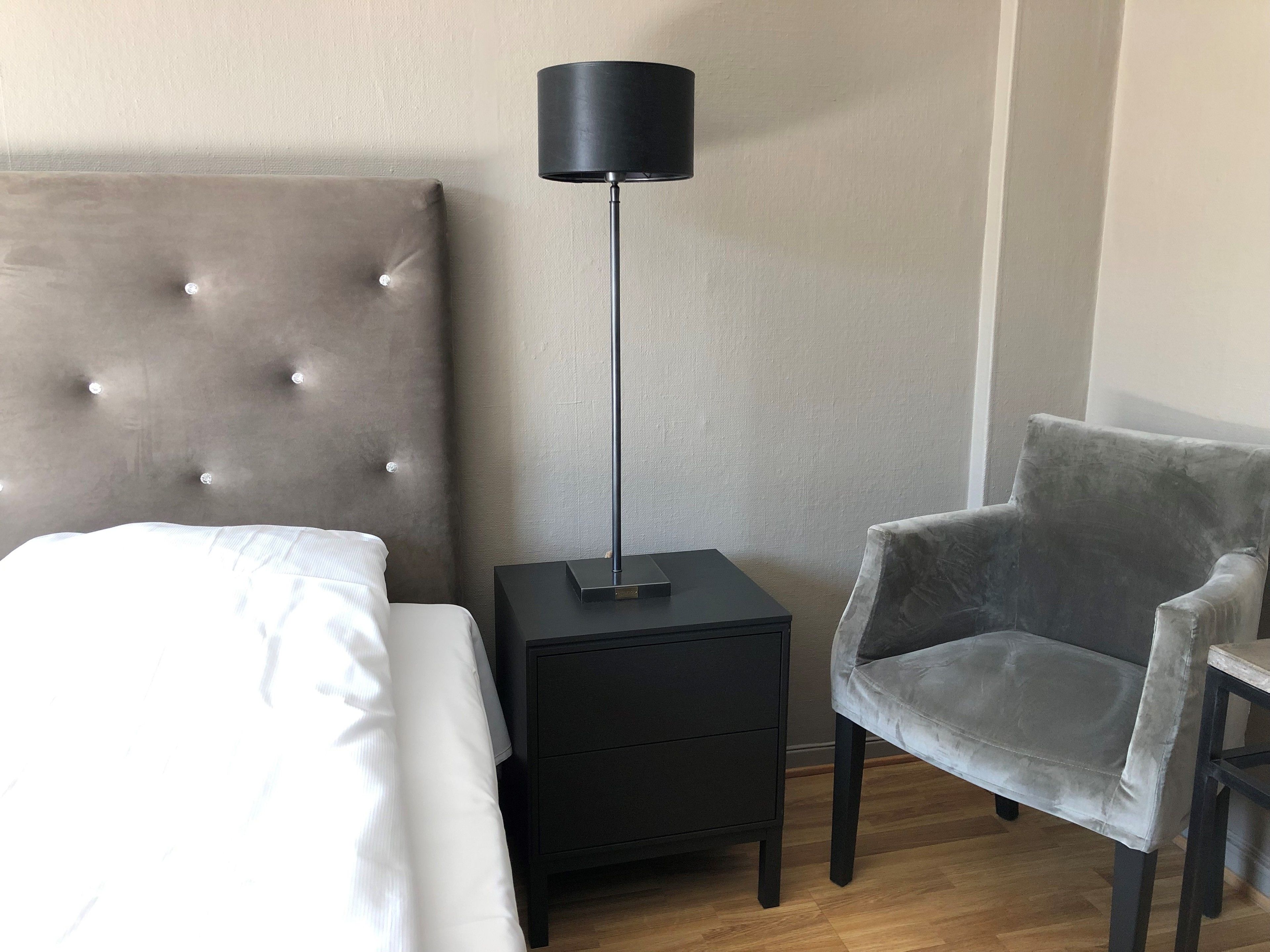 A hotel room with a bed, a nightstand, a lamp, and a chair.