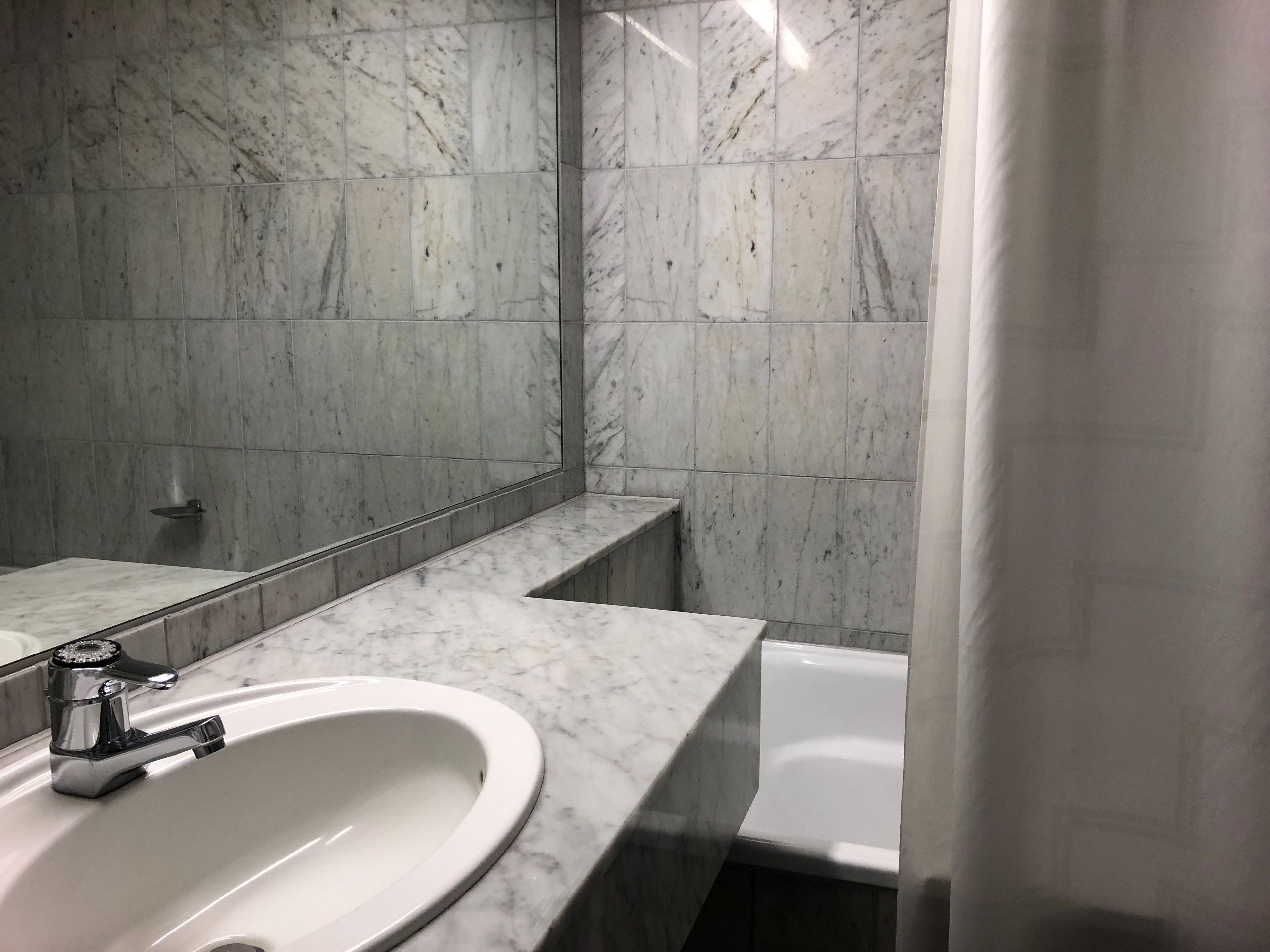 A bathroom with a marble sink, a mirror, and a shower curtain.