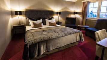 Ein Hotelzimmer mit einem großen Bett, zwei Nachttischen mit Lampen, einem kleinen runden Tisch, einer Couch und einem Fenster mit Vorhängen.